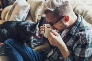 man, sofa, coffee, mug, coffee cup, cup, animal, drink, drinking coffee, morning coffee, coffee break, caffeine, drinking, adult, cat, pet, couch, indoors, leisure, portrait, seat, sitting
