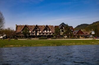 Picturesque hotel by the river with mountain backdrop, ideal for nature retreats.