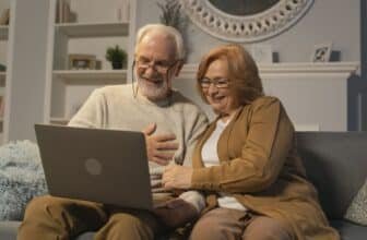 Happy senior couple sitting on a sofa having a joyful video call on a laptop in a cozy living room.
